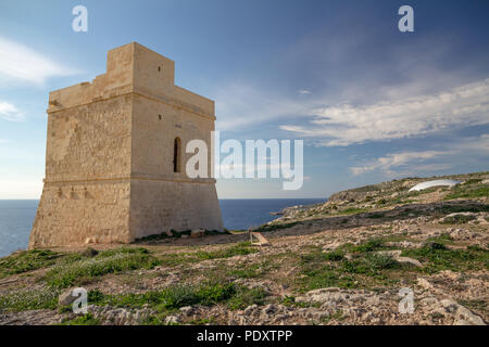 In soft light of winter afternoon, Tal Hamrija Coastal Tower near Hagar Qim, Malta, stands on coastal cliffs against blue skies and wispy skies Stock Photo