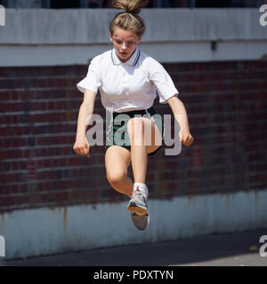 Teenage girl in mid air doing the  long jump for high school sports day Stock Photo