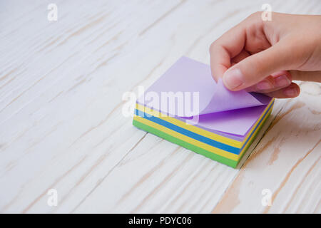 baby hand tears off sticker, colored sheets stickers on white wooden background. Stock Photo