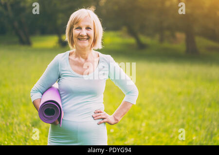 Portrait of sporty senior woman holding mat in the nature.Image is intentionally toned. Stock Photo