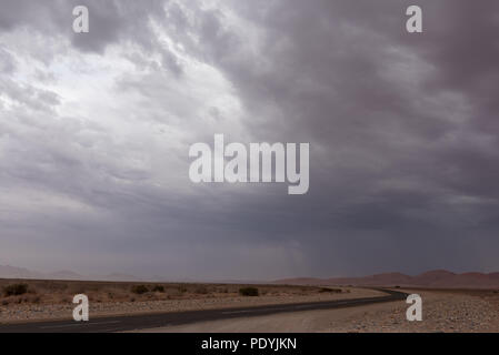 Dramatic thunderstorm rain and sandstorm over red sand dunes with asphalt road Stock Photo