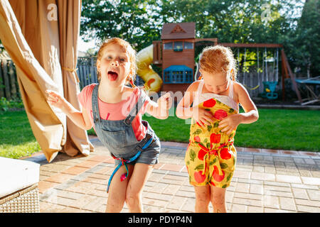 Portrait of  two little girls  sisters having fun on home backyard. Friends girls making silly faces. Lifestyle family moment of siblings playing toge Stock Photo
