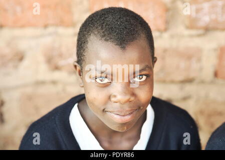 young Ugandan school children dressed in a school uniform sit outside on wooden benches studying for their exams with brick classroom in background Stock Photo