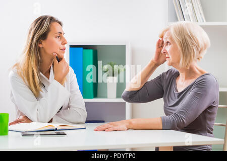 Senior patient telling female doctor how she is having headache. Stock Photo