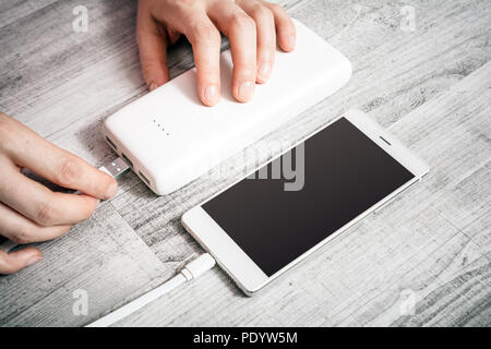 Female Hand Connecting Smartphone With Low Batteries With Powerbank To Recharge Energy, High Angle View Stock Photo