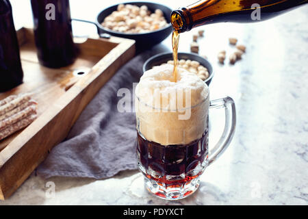 Glass of beer with snacks. Pouring beer from bottle into glass Stock Photo