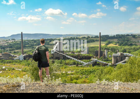 Person standing on a hillside overlooking the derelict building on the site of the former Cwm colliery and coke ovens in Beddau near Pontypridd. Stock Photo