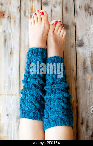 Woman's legs in knitted blue legwarmers closeup on wooden background. Stock Photo