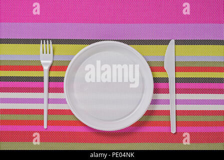 white plastic utensils, fork, plate and knife on a colored striped napkin Stock Photo