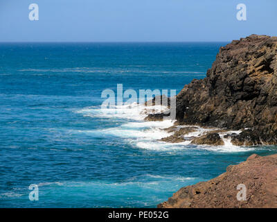 Waves crashing on rocks in bright sunshine Stock Photo