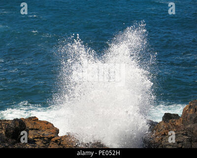 Waves crashing on rocks in bright sunshine Stock Photo