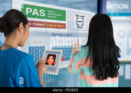 Female Patient using self registration system to check in while doctor find her medical record by digital tablet. Stock Photo