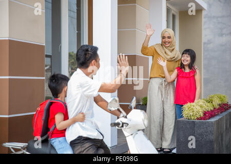 father and son on a scooter to take him to school. waving goodbye to mom and sister in front of the house Stock Photo