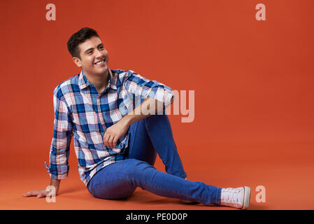 Young latin man sit on studio floor and looking up Stock Photo