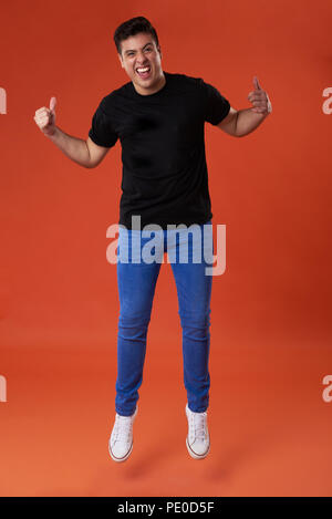 Jumping man with thumb up in orange studio background Stock Photo