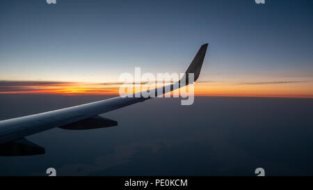 Right Wing of Airplane In Mid Air with Sunrise in the background Stock Photo