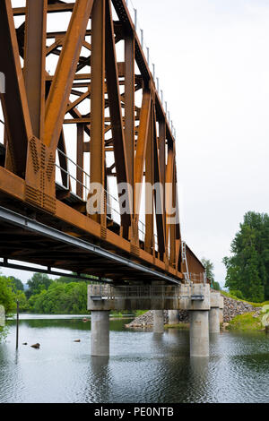 A new unpainted rusted metal truss railway bridge on concrete piles across the Washougal River in Camas Washington in national recreation Columbia Gor Stock Photo