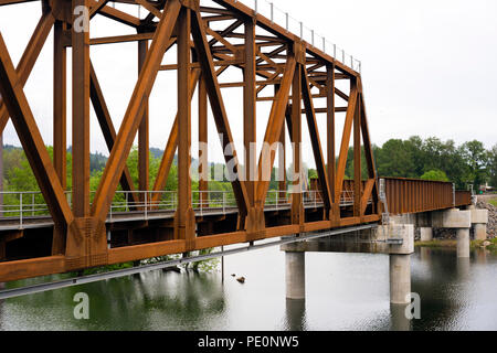 A new unpainted rusted metal truss railway bridge on concrete piles across the Washougal River in Camas Washington in national recreation Columbia Gor Stock Photo