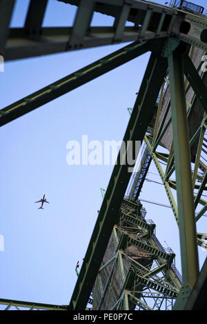 An airplane in the sky flies over Columbia Interstate lifting bridge with towers with concrete counterweights to raise the lifting part of the bridge  Stock Photo