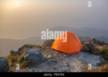 orange tent camping near cliff isolated on lantau peak, Hong Kong in sunrise and fog with copy space Stock Photo