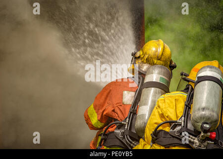 close up action of two firefighters water spray by high pressure nozzle to fire and  smoke with  copy space in cinematic tone Stock Photo
