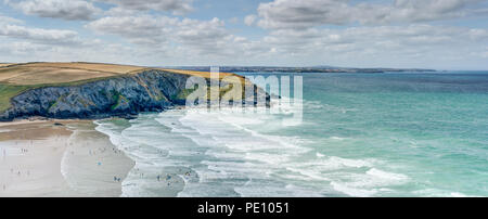 A wide panoramic landscape of Mawgan Porth Beach, Cornwall, famous for it's aqua blue sea, yellow sand and white surf. Newquay is in the distance. Stock Photo