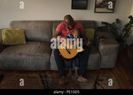 Father and son playing with guitar in living room Stock Photo