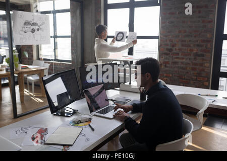 Businessman using laptop while his colleagues looking at sketch Stock Photo