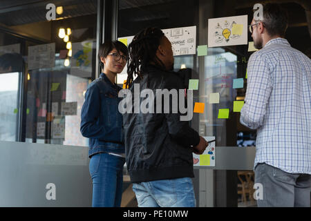 Executives discussing over sticky notes on glass wall Stock Photo