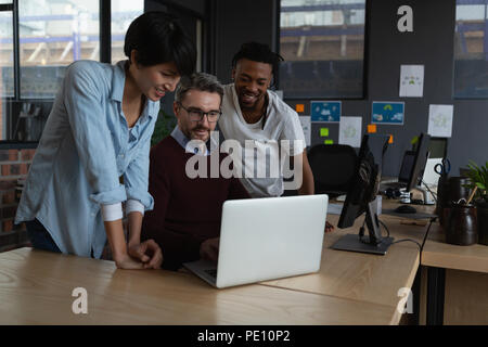 Executives discussing over laptop at desk Stock Photo