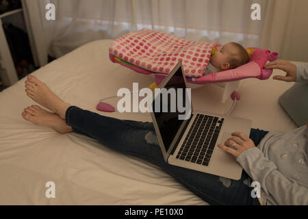 Mother using laptop while her baby boy sleeping Stock Photo