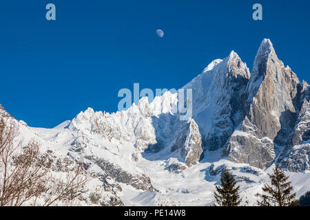 The moon against a deep blue sky above the mountains near Chamonix.  Chardonnay and and Les Drus are covered in snow.  Taken from Montroc Stock Photo