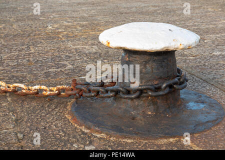 Mooring bollard with rusty chain fastened around it on a quay in a harbour Stock Photo