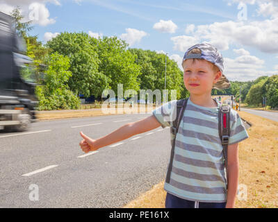 Day view little child boy traveller with backpack catching car on UK road. Stock Photo