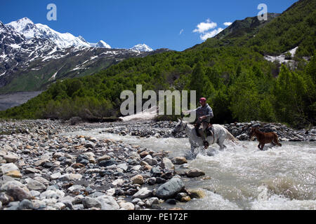 Man on a horse crossing a river in Caucasus mountains in Svaneti, Georgia