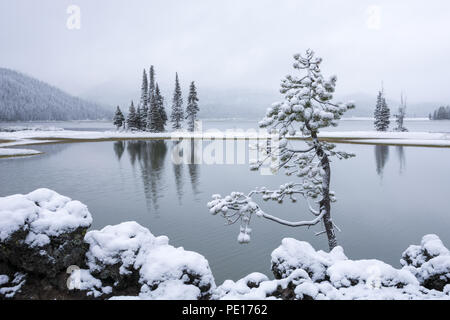 A light snowfall covers the trees, rocks, and mountains surrounding Sparks Lake in Central Oregon on an early morning in June. Stock Photo