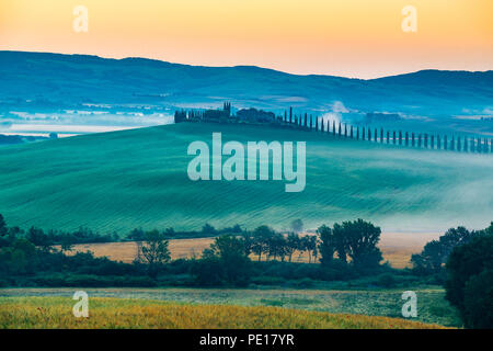 Beautiful landscape of the Tuscany in the early morning with the green hilly field the farm house and the line of Cypress trees Stock Photo