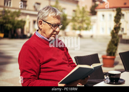 Senior man enjoys reading book and drinking coffee at the bar. Stock Photo