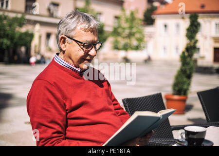 Senior man enjoys reading book and drinking coffee at the bar. Stock Photo