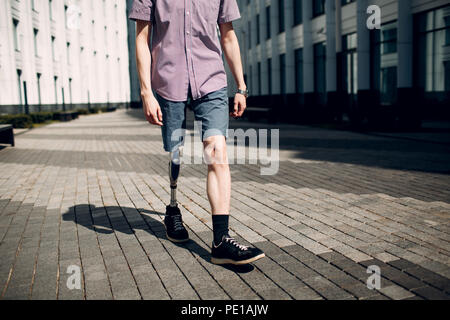 Disabled young man with foot prosthesis walks along the street. Stock Photo