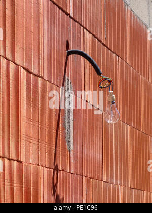 Single light bulb hanging from a wire on the exterior of a newly built wall at a house in Cessenon-sur-Orb, France Stock Photo