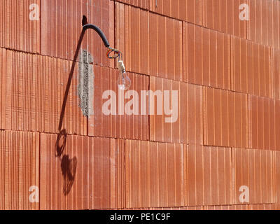 Single light bulb hanging from a wire on the exterior of a newly built wall at a house in Cessenon-sur-Orb, France Stock Photo