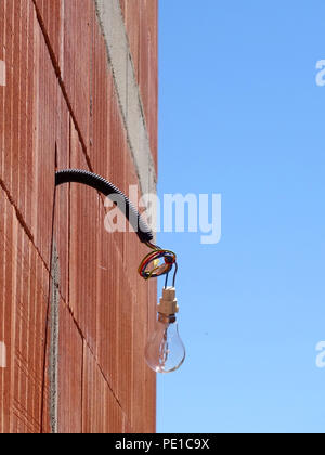 Single light bulb hanging from a wire on the exterior of a newly built wall at a house in Cessenon-sur-Orb, France Stock Photo