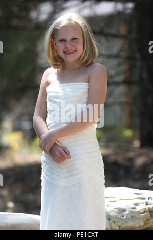 Fantasy, 8-9 year attractie blonde, wearing aunt's wedding dress. Standing outdoors smilimg at camera. Stock Photo