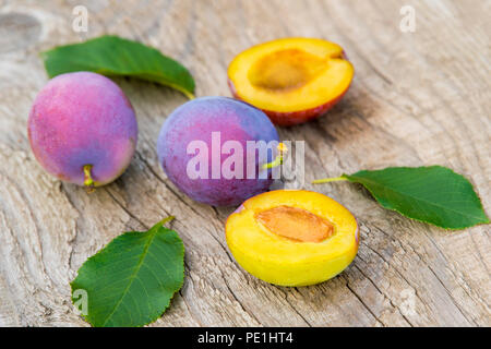 ripe plums with leaves on old wooden background Stock Photo
