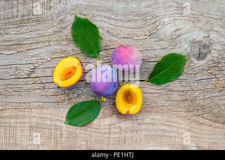 ripe plums with leaves on old wooden background Stock Photo
