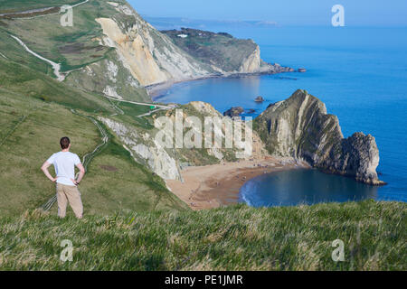 Middle aged man with his hands on his hips, looking down at a coastal view of Durdle Door on the Jurassic Coast in South England