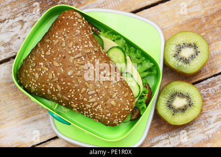 Healthy school lunch box containing brown cheese roll and kiwi fruit Stock Photo