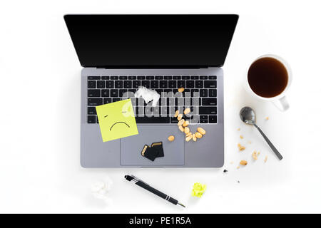 Top view of tabletop with messy dirty laptop, post it notes with sad face, nuts, memory cards, pen, spoon and coffee cup isolated on white background Stock Photo