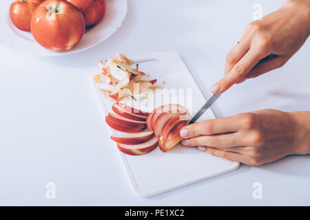 Close-up woman's hands slicing apples on white table near plate with whole red fruits, top view. Stock Photo